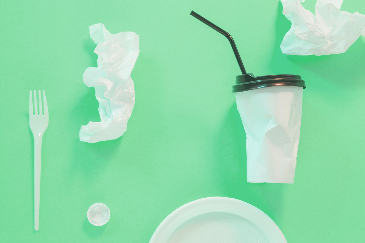 crumpled up pieces of trash -- a plastic cup, straw, plastic fork, plastic soda bottle cap, paper, plate, on a green background. 888 has helped remove approximately 130 kilograms of plastic from circulation by utilizing biodegradable poker chip bags.