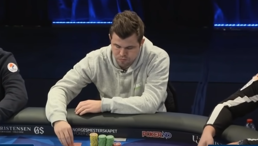 a disheartened white male in a grey hoodie scowls down at the poker table. he has playing cards face down and a stack of green and yellow poker chips on the table in front of him.