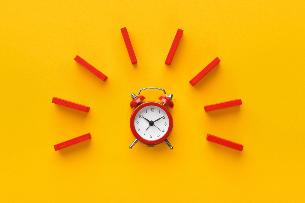 A vintage red alarm clock on a yellow background. Around the clock are red lines created by dominoes that allude to the alarm going off, alerting players to the huge overlays at 888poker Ontario right now.